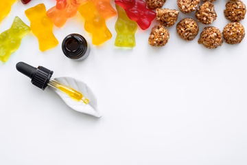 Assorted colorful gummies, dropper bottle, and snack bites on white background