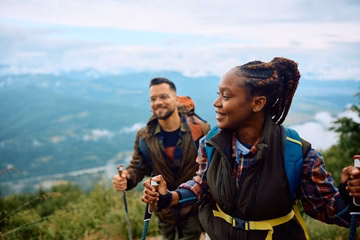 woman and man on a hillside hiking with walking sticks and backpacks