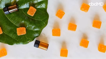 Orange CBD gummies and tincture bottles on a green leaf and white background