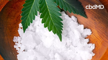 CBD isolate crystals in a wooden bowl with hemp leaves, illustrating pure CBD extract.