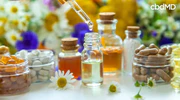 CBD tincture dropper above glass bottle, surrounded by capsules, vitamins, and flowers