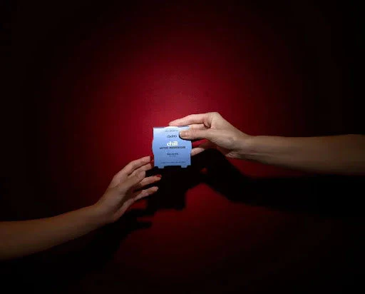 Two hands exchanging a blue relax supplement box against a dark red background