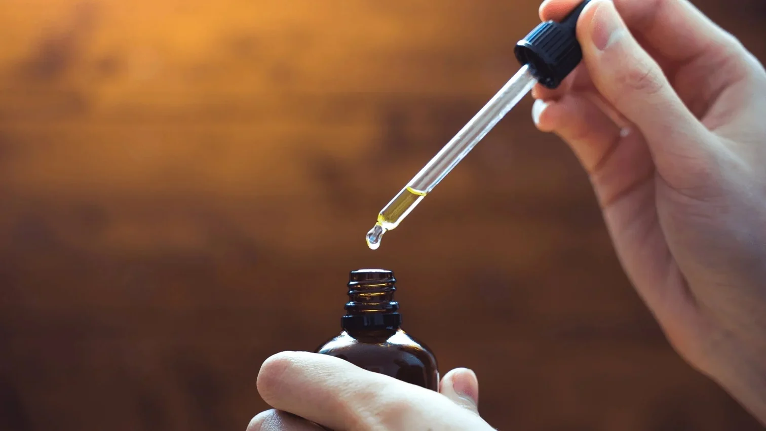 close-up of a hand holding a dropper with cbd oil over a tincture bottle