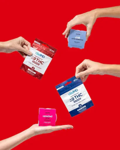Hands holding assorted wellness gummies in colorful packaging against a bright red background