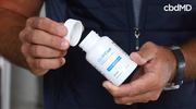 Man opening cbdMD pain relief capsules bottle, close-up of hands and product label
