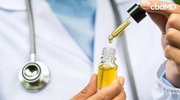 Doctor holding a CBD oil dropper bottle with stethoscope visible, close-up