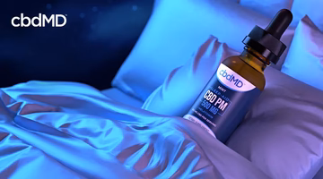 CBD PM oil dropper bottle on blue bed sheets, sleep aid supplement for better rest