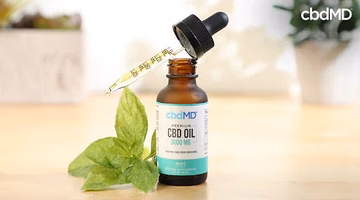 Bottle of CBD oil with dropper and mint leaves on light wooden surface