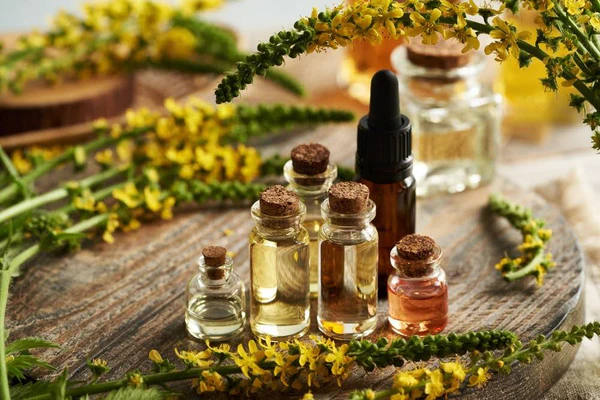 Assorted essential oil bottles with dropper on wooden surface, surrounded by yellow flowers