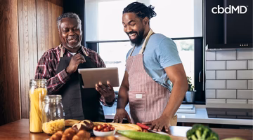 Father and son in aprons cooking healthy meal together using a tablet in modern kitchen