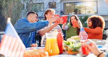 group of friends toasting cups at an outdoor feast for the Fourth of July 