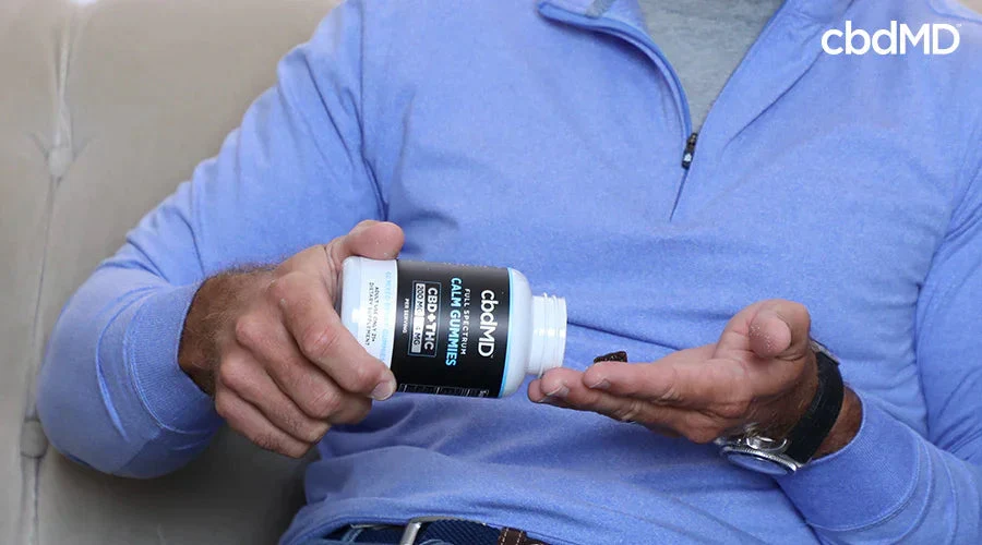 Man in blue shirt pours CBD calm gummies from bottle into hand while sitting on couch
