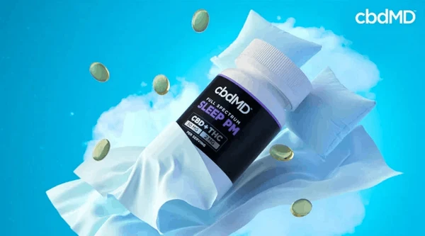 cbdMD Sleep PM bottle graphic between sheets and pillows against a blue background