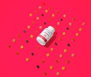 White bottle of gummies with assorted cube-shaped gummies scattered on vibrant pink background
