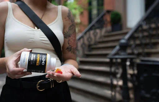Person holding CBD gummies bottle and pouring gummies into hand on outdoor stairs