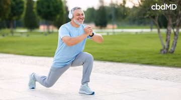 Active older man doing outdoor lunge exercise, wearing headphones and fitness attire on a sunny day