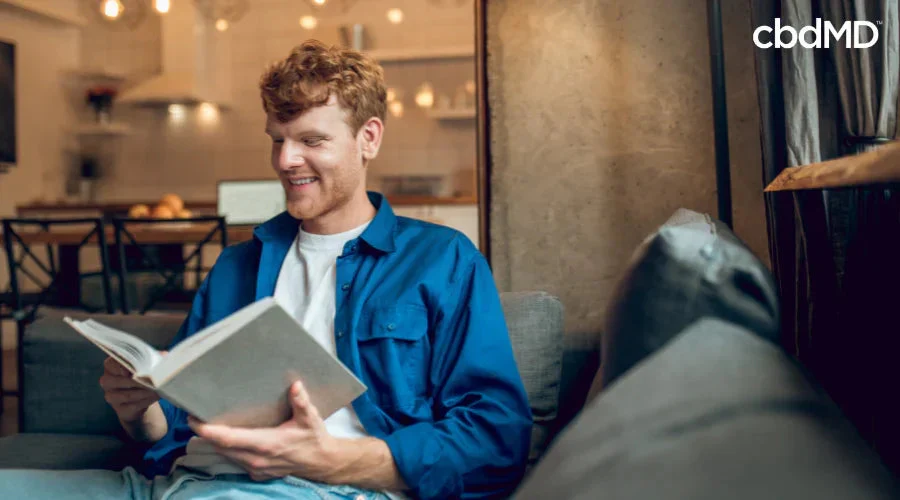 Smiling man in casual clothing relaxing at home and reading a book in a cozy living room