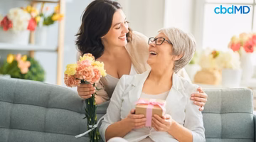 Happy mother and daughter celebrating Mother's Day with flowers and a gift on a couch