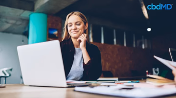 Smiling woman focusing on work at desk with laptop and papers in modern office setting
