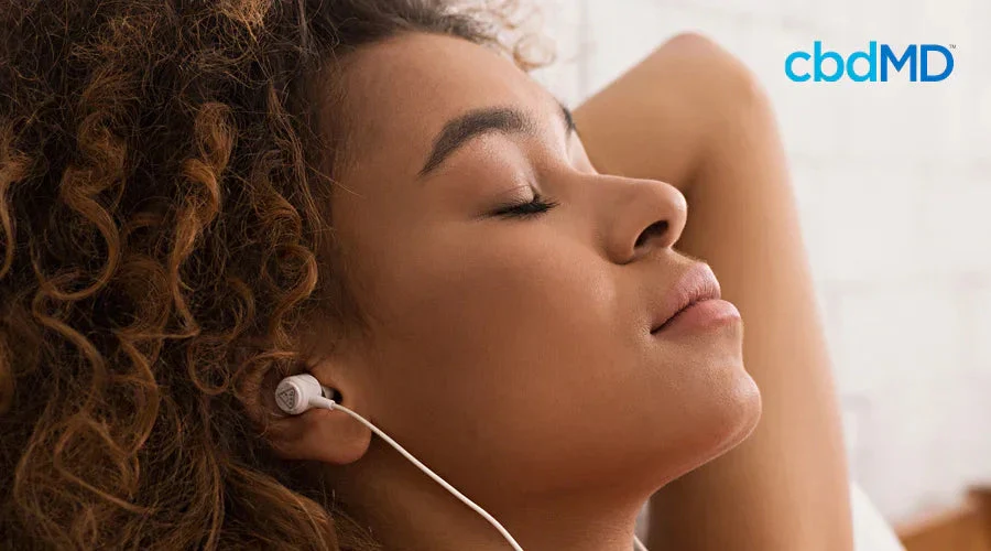 Woman relaxing with eyes closed, listening to music with earbuds in a calm indoor setting.