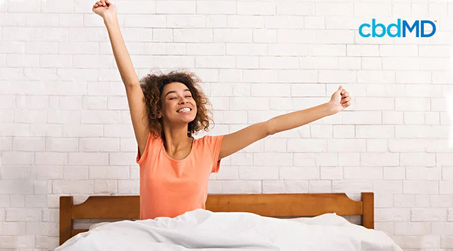 Smiling woman stretching in bed after waking up, white brick wall background
