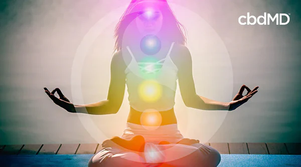 Woman meditating outdoors with colorful chakra symbols overlay, promoting wellness and balance