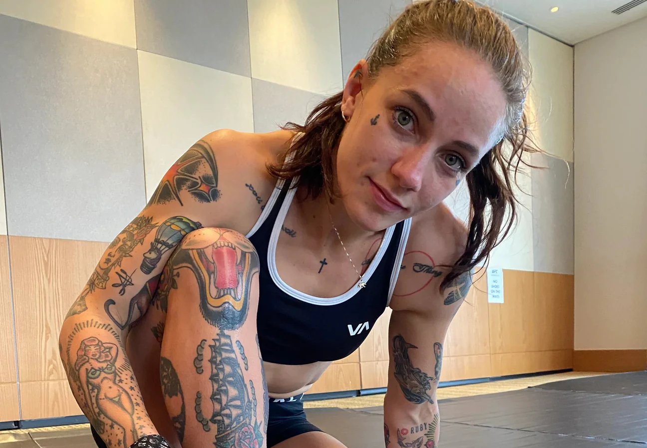Tattooed female athlete in black sportswear kneeling on a mat indoors
