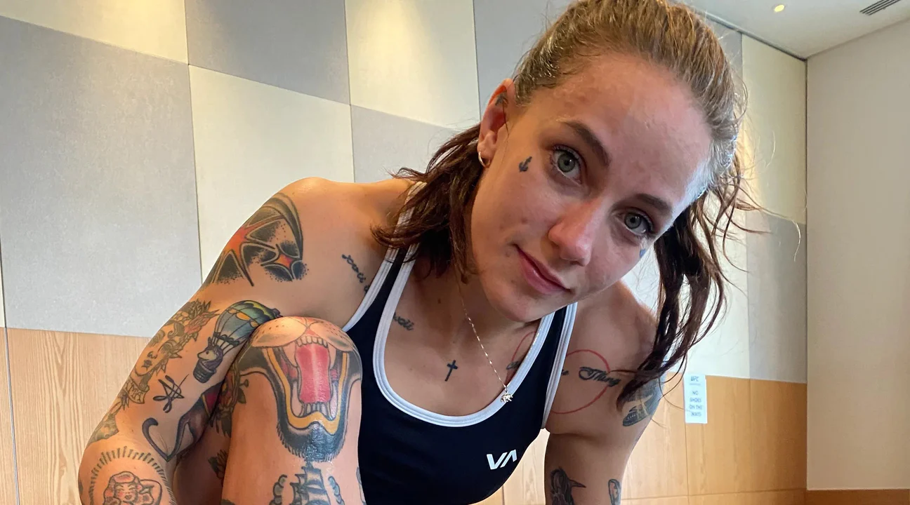 Athletic woman with tattoos in gym attire posing indoors, close-up after workout