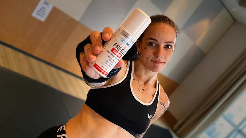 Athletic woman in sportswear holding CBD topical freeze roller for muscle recovery indoors