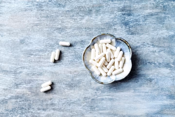 White supplement capsules in a decorative bowl on a blue textured surface