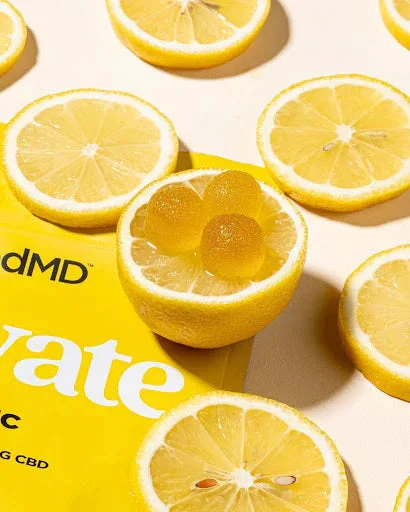 Lemon slices and yellow gummy supplements on a bright surface, with product packaging partially visible.