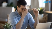 Stressed man at desk holding glasses, massaging nose bridge, laptop in front