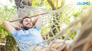 Smiling man relaxing in a hammock outdoors, sunlight, cbdMD logo in corner