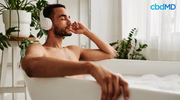 Man relaxing in a bubble bath, wearing headphones, surrounded by houseplants, self-care concept