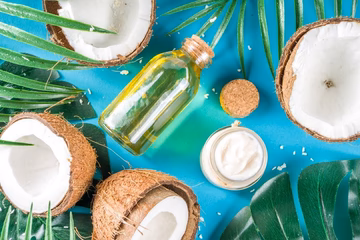 Coconut halves, coconut oil bottle, and cream jar on blue background with palm leaves