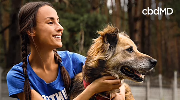 Smiling woman outdoors hugging happy large dog, promoting pet wellness lifestyle.