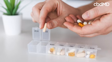 Person placing CBD capsules and supplements into weekly pill organizer