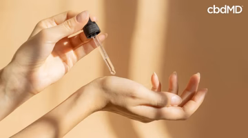 Person applying CBD oil to skin with dropper for skincare wellness