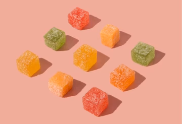Assorted fruit-flavored gummies with sugar coating on a pink background