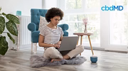Woman relaxing at home on a rug with laptop, cup, and cozy decor in natural light living room