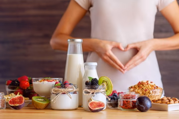 Assorted whole foods including yogurt, milk, berries, figs, kiwi, granola, and nuts for gut health