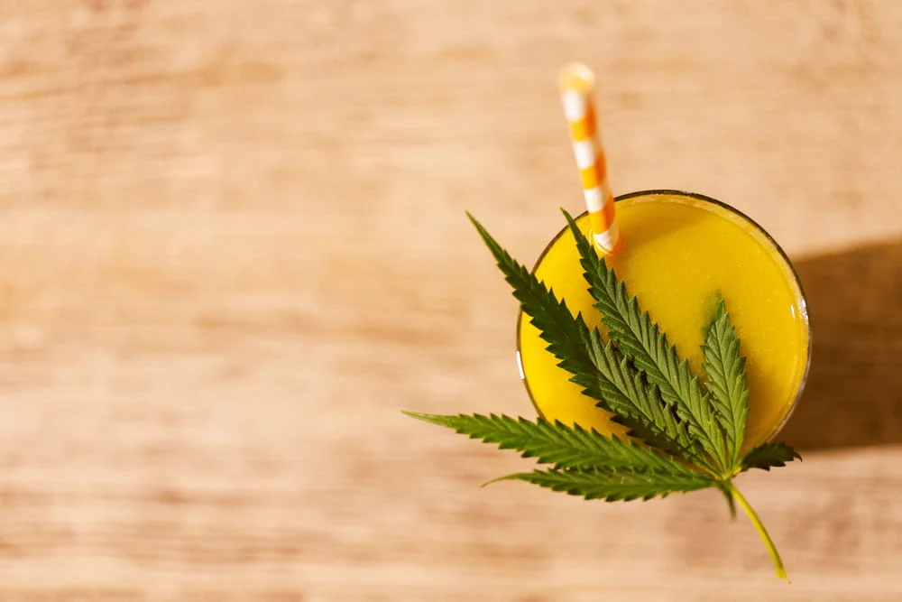 orange drink with a straw topped off with a hemp leaf