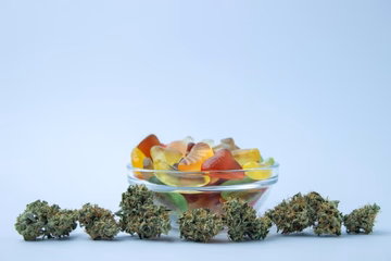 Bowl of colorful gummies with hemp flower buds on white background