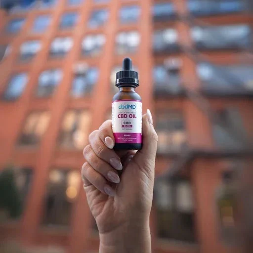 Hand holding CBD oil tincture bottle outdoors with blurred brick building background