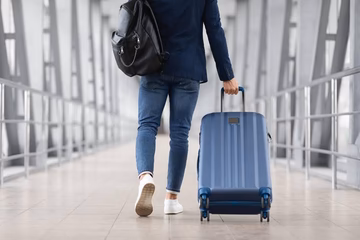 Traveler walking in airport with blue rolling suitcase and black backpack