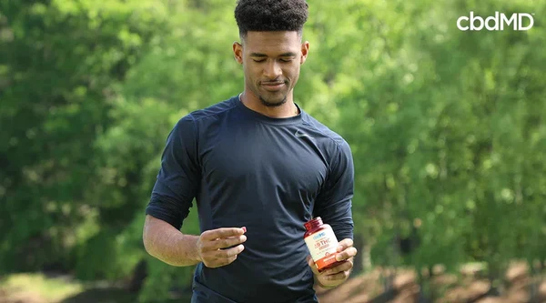 runner in a field holding a bottle in one hand and a delta 9 gummy in the other