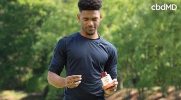 man in a field holding a cbdMD bottle in one hand and a delta 9 gummy in the other