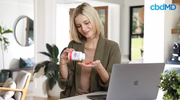 woman sitting at a desktop and placing cbd gummies from a bottle in the palm of her hand