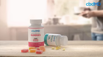 CBD gummies and softgel capsules on a kitchen counter with a blurred person in the background