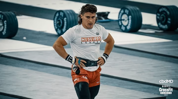 Male athlete in CrossFit event, wearing a lifting belt, weights in background, indoor gym